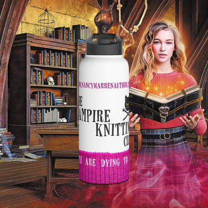 A white insulated water bottle with a black lid stands in front of a fantasy-style bookshop scene. The bottle has a black and pink printed design with the text 'The Vampire Knitting Club' and 'People are dying to join.'